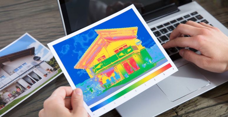 Zdjęcie termowizyjne domu trzymane w ręku na tle laptopa
